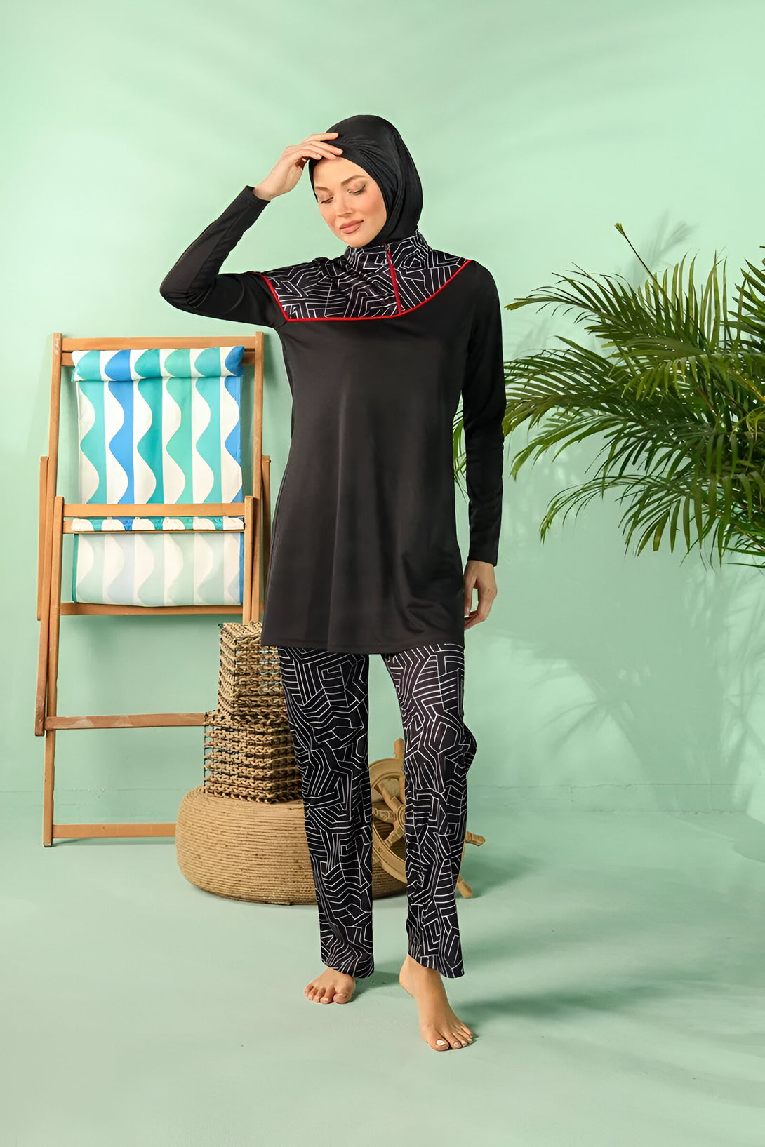 Une femme portant un maillot de bain musulman noir avec des détails blancs et une ligne rouge. Elle porte également un hijab noir. La photo a été prise sur fond vert.