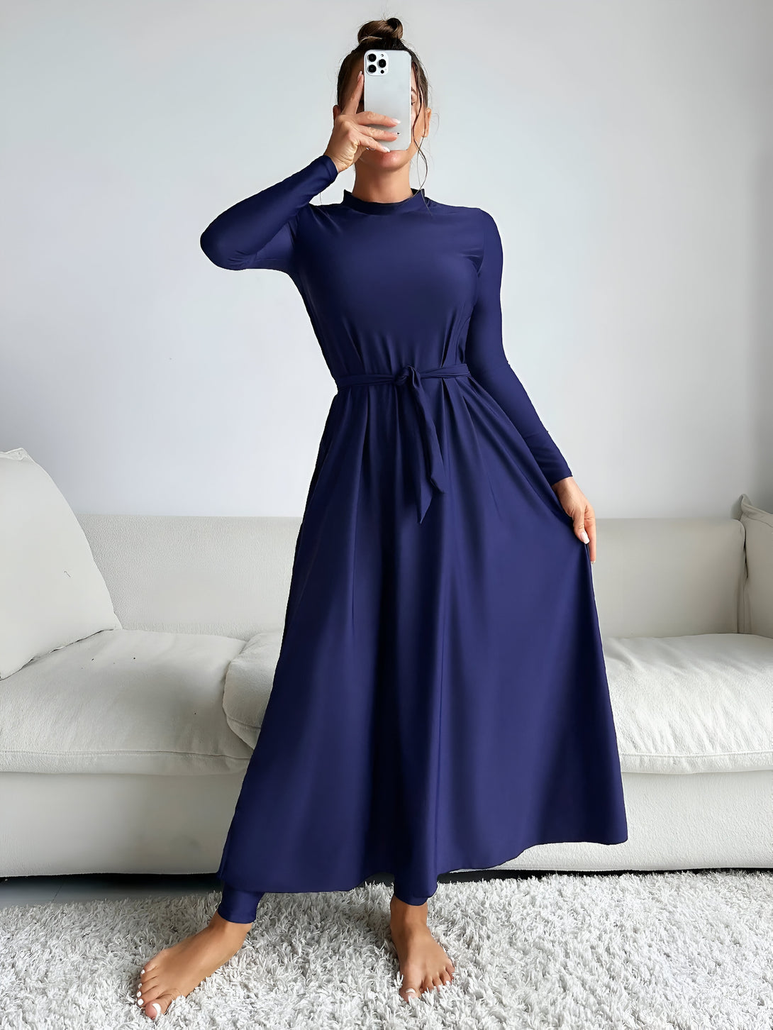 Une femme porte une robe longue bleu marine avec une ceinture. La robe est ample et fluide. Elle est idéale pour les occasions spéciales ou pour le quotidien.