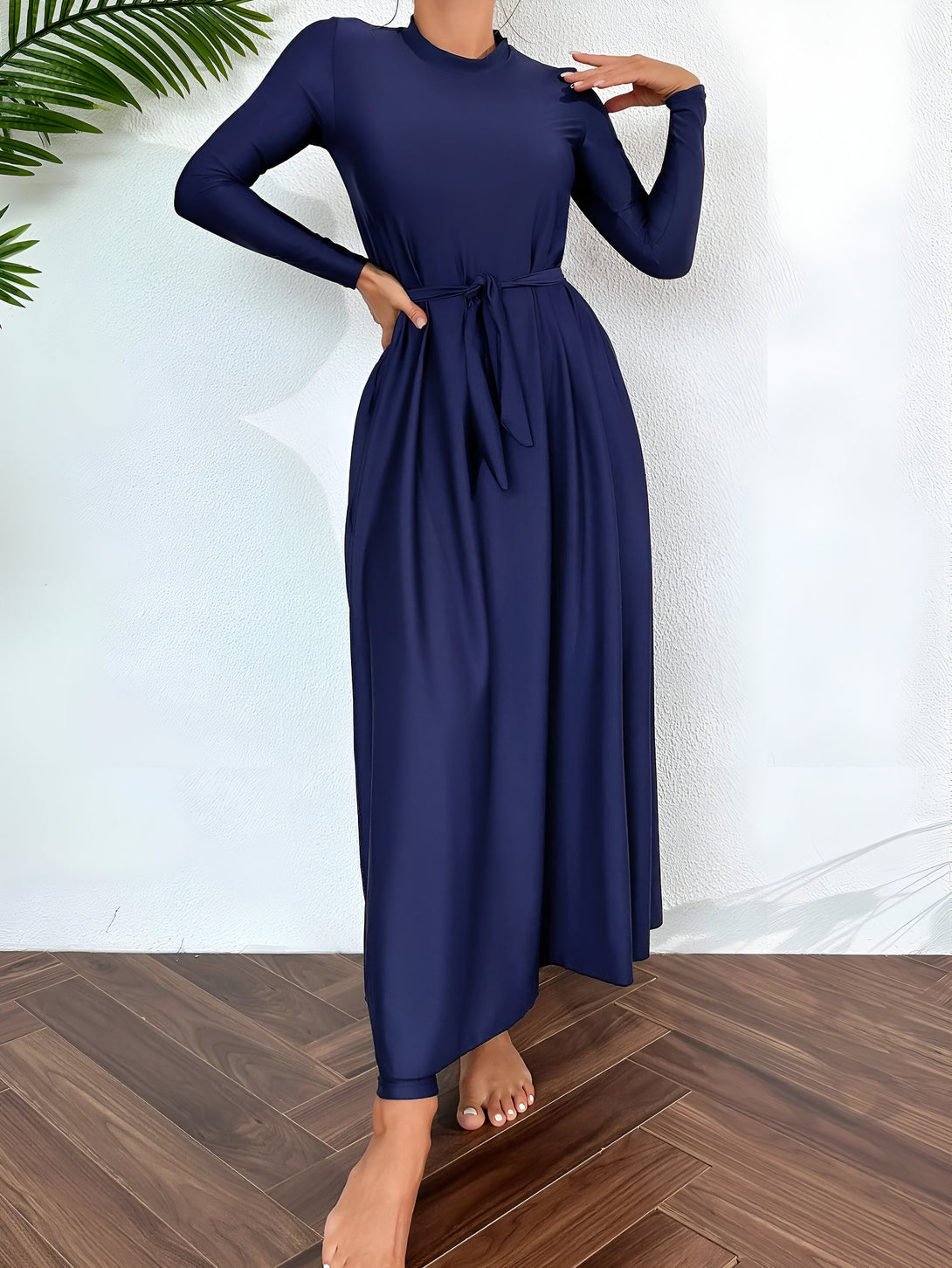 Une femme portant une robe longue bleu marine à manches longues avec une ceinture nouée à la taille. La robe est ample et fluide, idéale pour un look élégant et confortable.