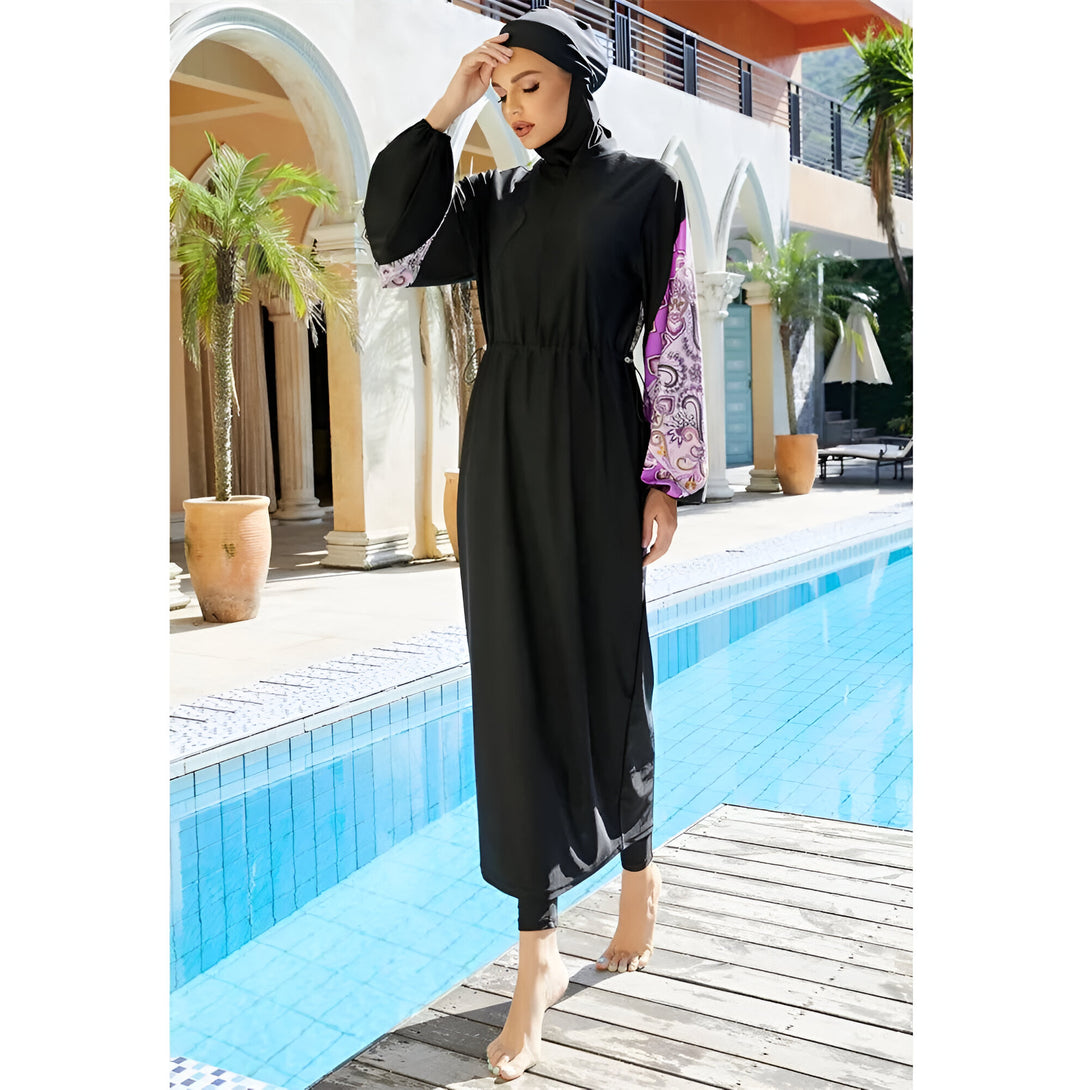 Une femme portant un maillot de bain musulman noir à manches longues et des motifs floraux violettes sur les poignets, près d'une piscine.