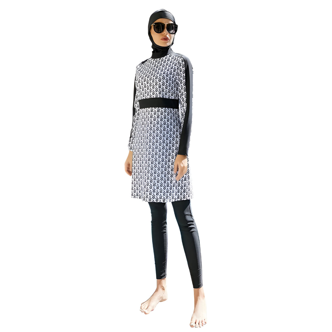 Une femme portant un maillot de bain musulman noir et blanc avec un motif floral. Le maillot de bain a des manches longues et des leggings. La femme porte un hijab noir et des lunettes de soleil.