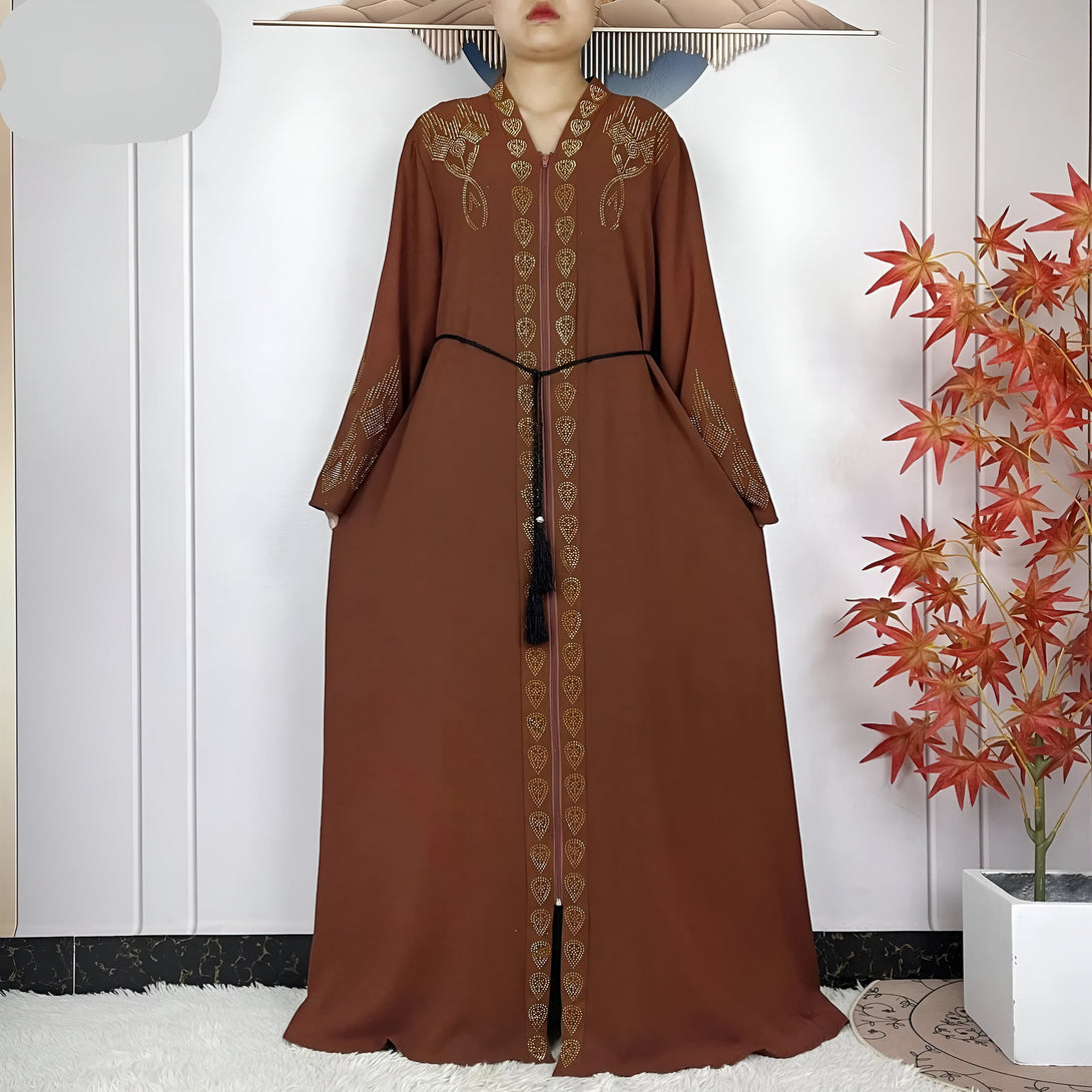 Une magnifique abaya marron avec des détails dorés et une ceinture noire. L'abaya est ornée de motifs en forme de goutte d'eau sur les côtés. Elle est parfaite pour les occasions spéciales.