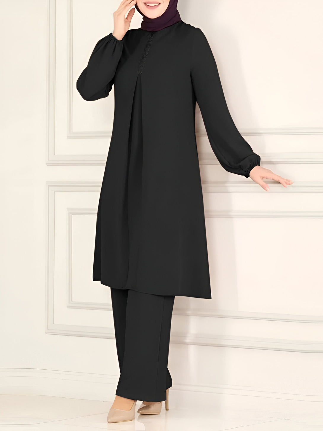 Une femme portant un ensemble noir composé d'un chemisier à manches longues et d'un pantalon. Le chemisier est décoré d'une fermeture boutonnée sur le devant et de détails de dentelle. Le pantalon est large et confortable.