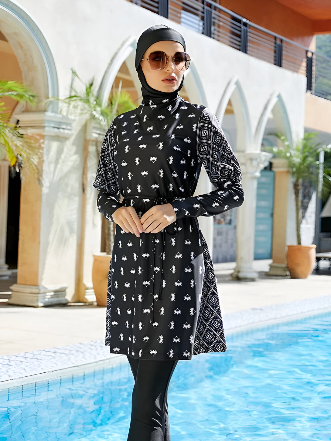 Une femme portant un maillot de bain musulman noir et blanc à motifs floraux, se tenant près d'une piscine.