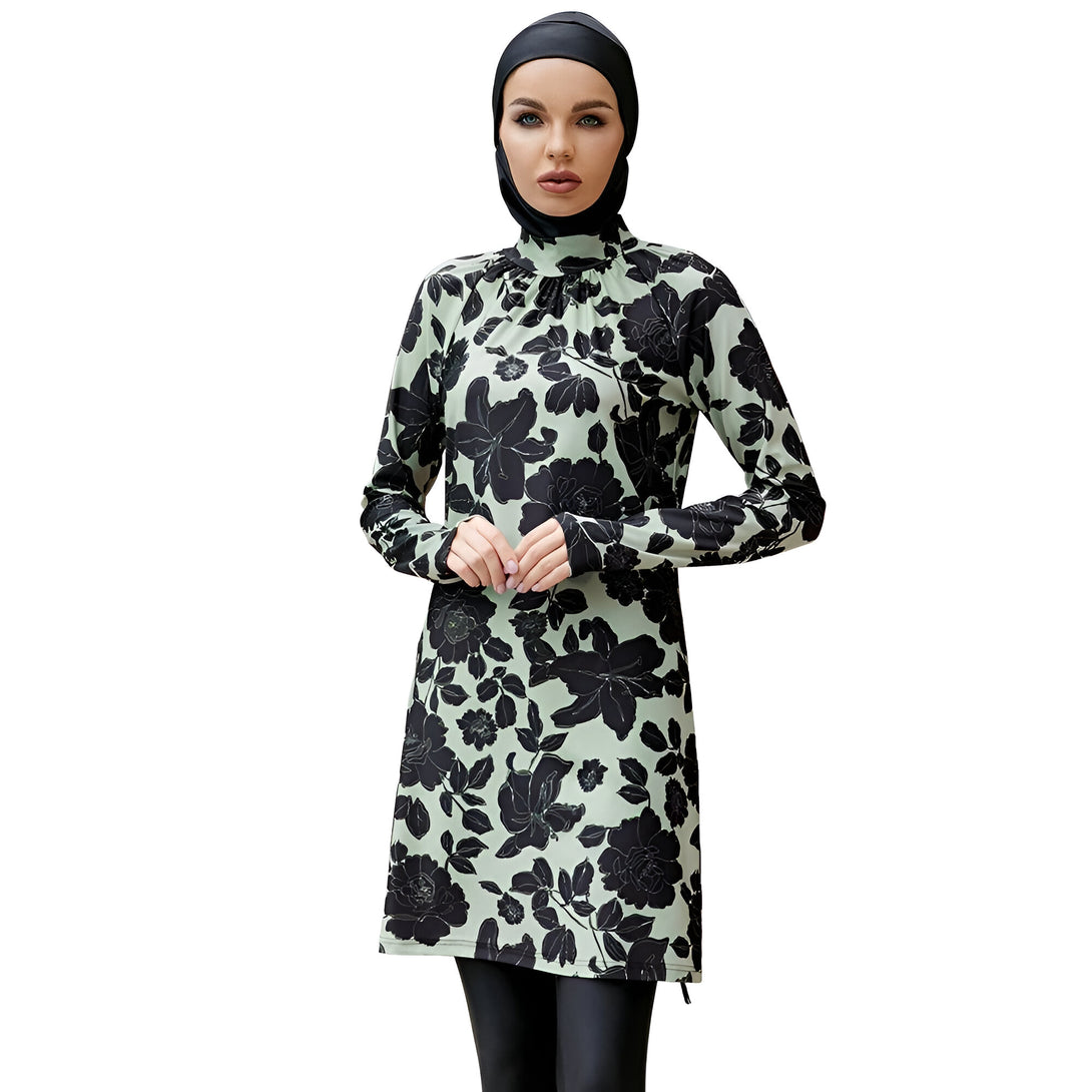 Une femme portant un maillot de bain musulman vert clair avec un motif floral noir. Le maillot de bain comprend une tunique à manches longues et un pantalon long. La femme porte également un hijab noir.