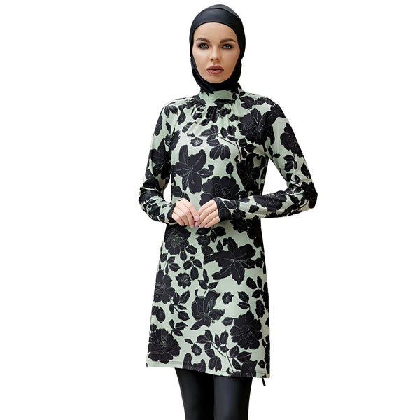 Une femme portant un maillot de bain musulman vert clair avec un motif floral noir. Le maillot de bain comprend une tunique à manches longues et un pantalon long. La femme porte également un hijab noir.