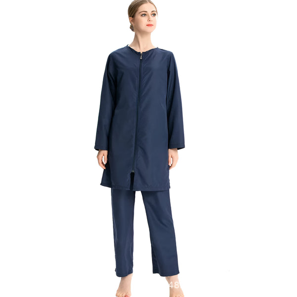 Une femme porte un ensemble de vêtements de bain musulmans bleu marine. La tenue comprend une robe longue à manches longues avec une fermeture éclair sur le devant et un pantalon coordonné.