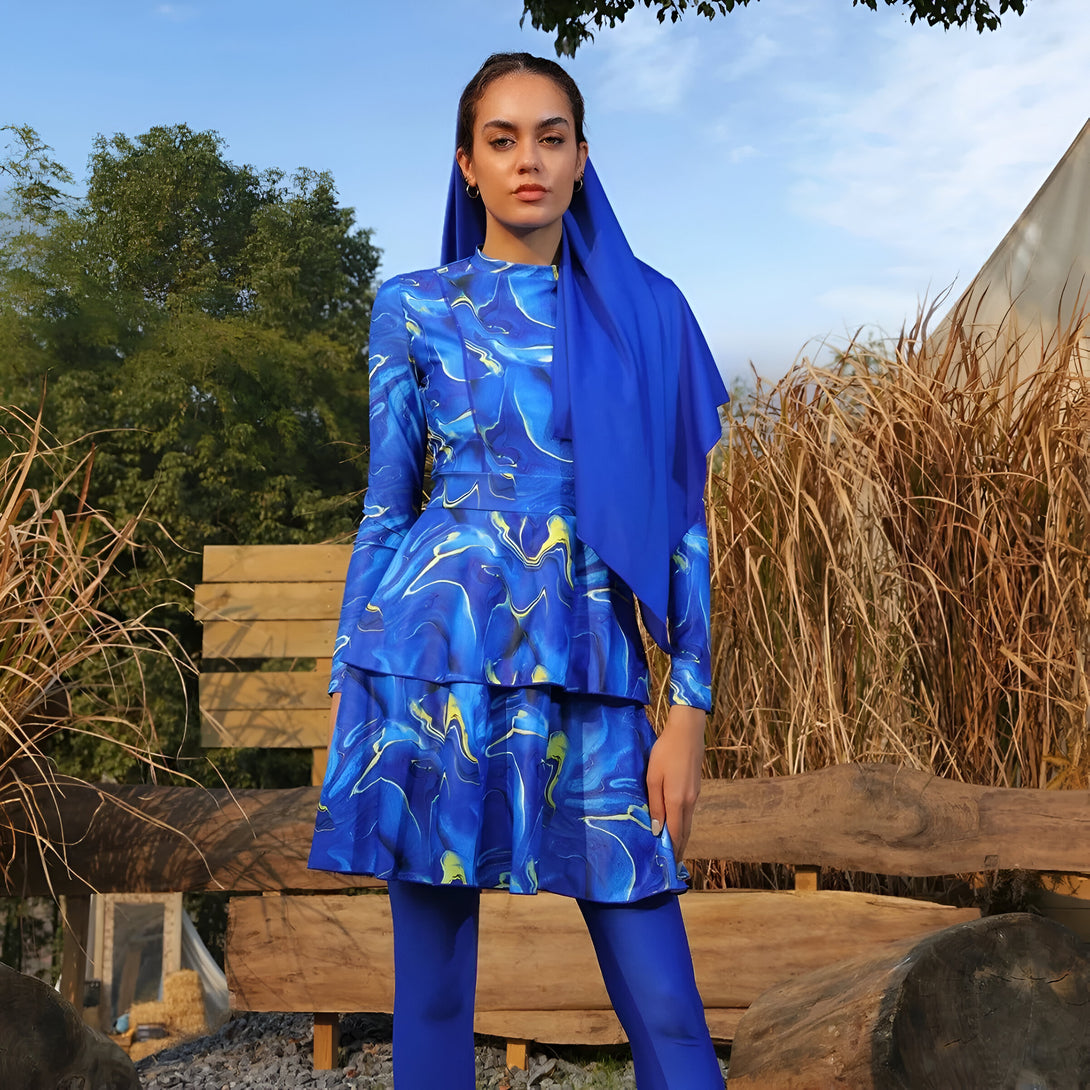 Une femme portant un hijab bleu et une combinaison de bain musulmane bleue à imprimé marbré. La tenue est élégante et confortable, idéale pour la natation ou la plage.