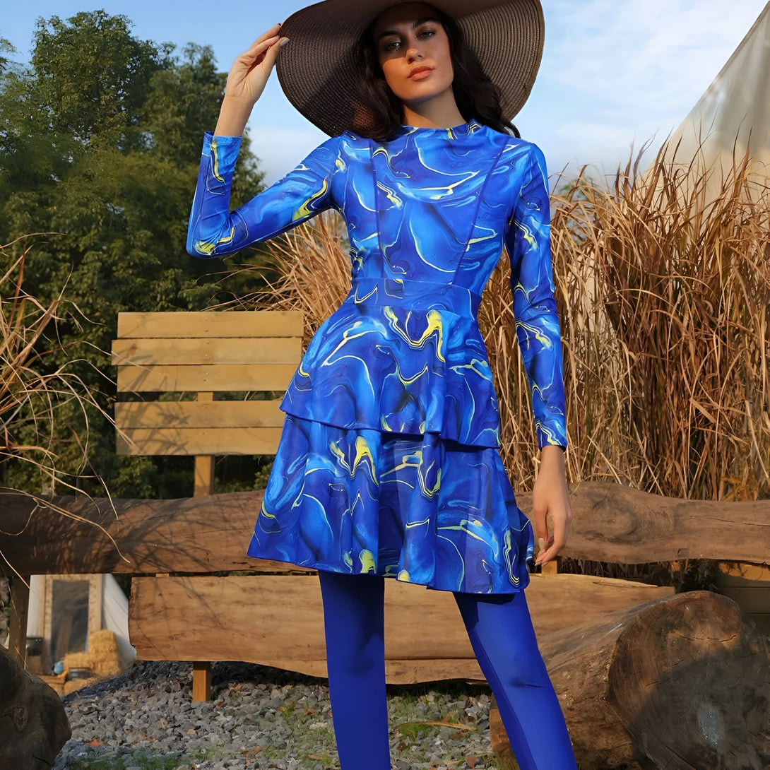 Une femme portant une robe de bain musulmane bleue à manches longues avec un motif marbré. Elle porte également un chapeau de paille brun.