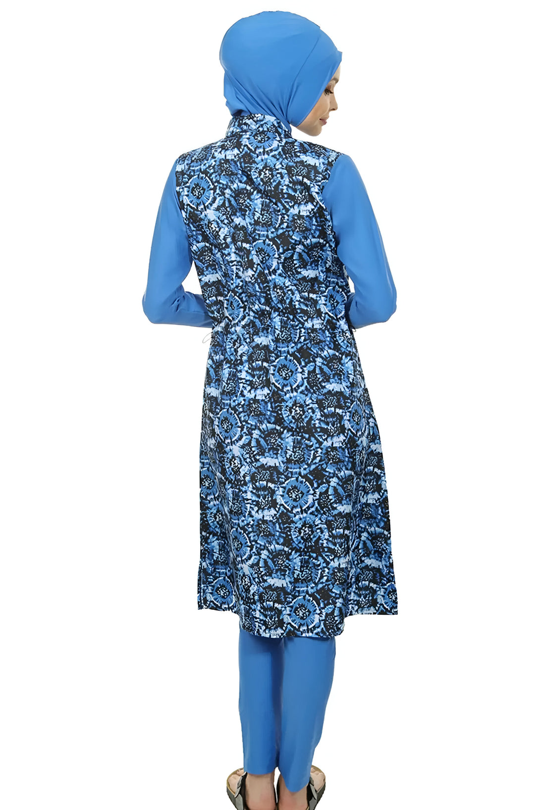 Une femme portant un maillot de bain musulman bleu avec un motif floral. Le maillot de bain est à manches longues et couvre tout le corps, sauf les pieds et les mains. La femme porte un foulard bleu sur la tête.