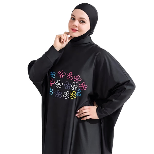 Une femme portant un maillot de bain musulman noir avec des fleurs multicolores brodées.  Le maillot de bain est à manches longues et a un col haut. La femme porte également un foulard assorti.
