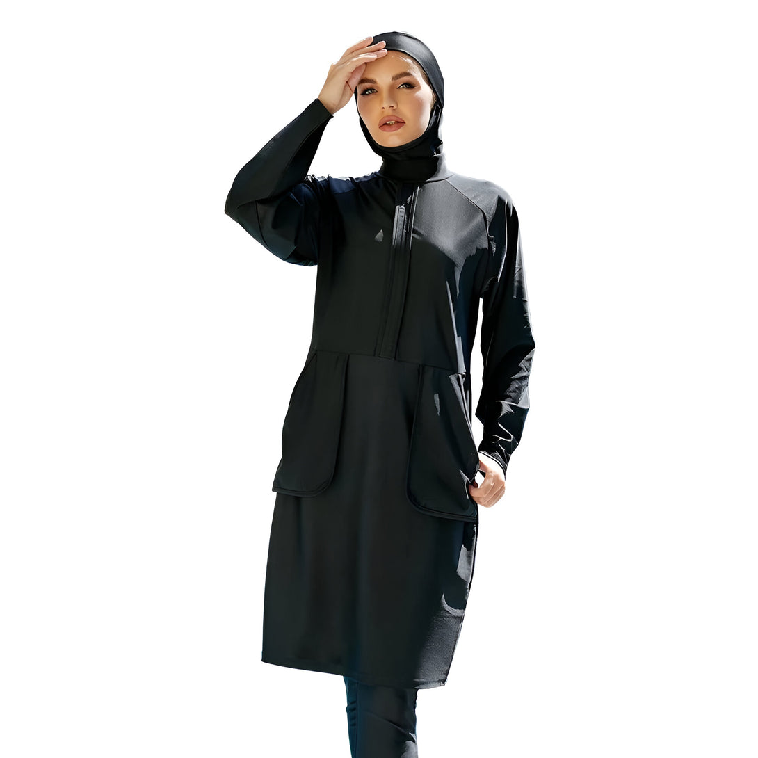 Une femme portant un maillot de bain musulman noir avec une fermeture éclair sur le devant et des poches. Le maillot de bain est long et couvre tout le corps. La femme porte également un hijab noir.