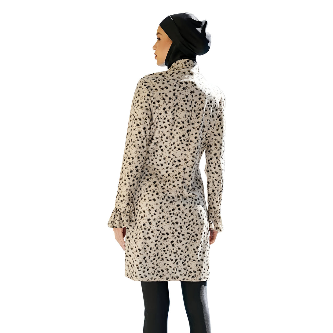 Une femme portant une robe longue à manches longues avec un motif floral et un hijab noir. La robe est beige et le hijab est noir. La femme est vue de dos et porte un pantalon noir.