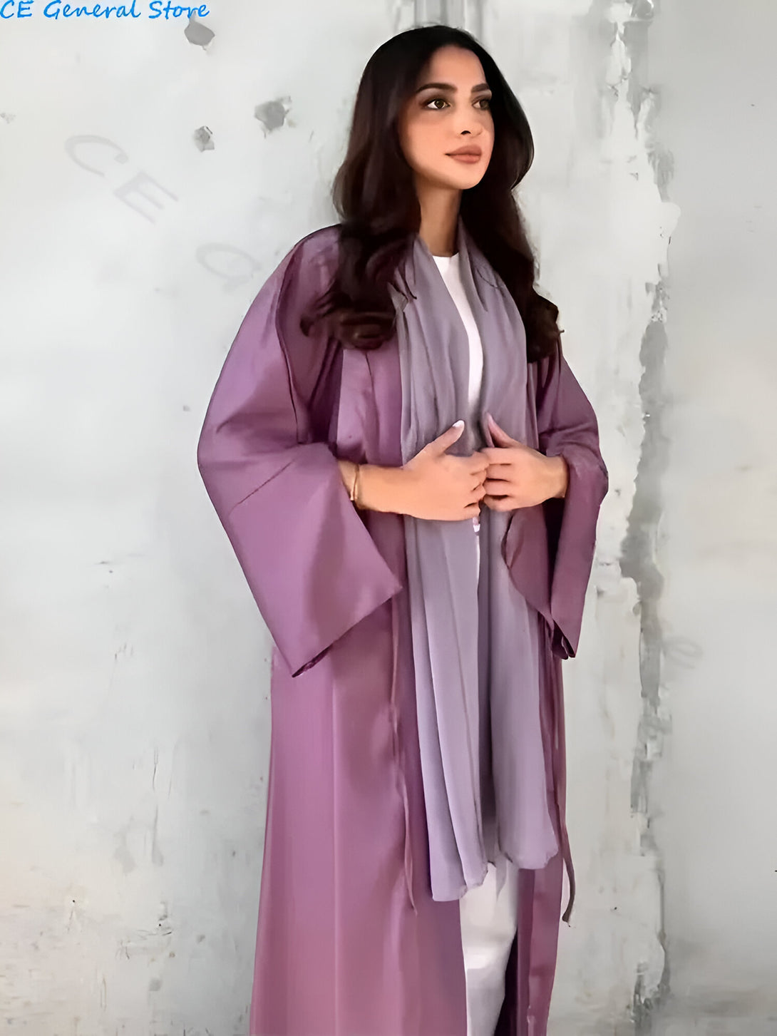 Une femme portant une abaya violette élégante et un hijab gris.  Le tissu est doux et fluide, parfait pour une occasion spéciale.  Achetez votre abaya aujourd'hui!