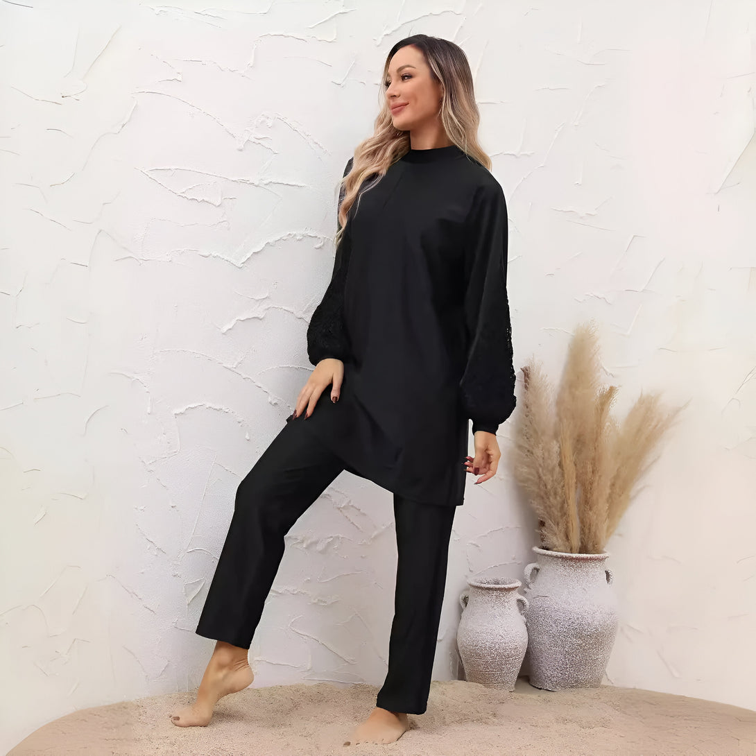 Une femme porte un ensemble de vêtements de bain musulman noir avec des manches en dentelle. L'ensemble comprend un haut à manches longues et un pantalon long.