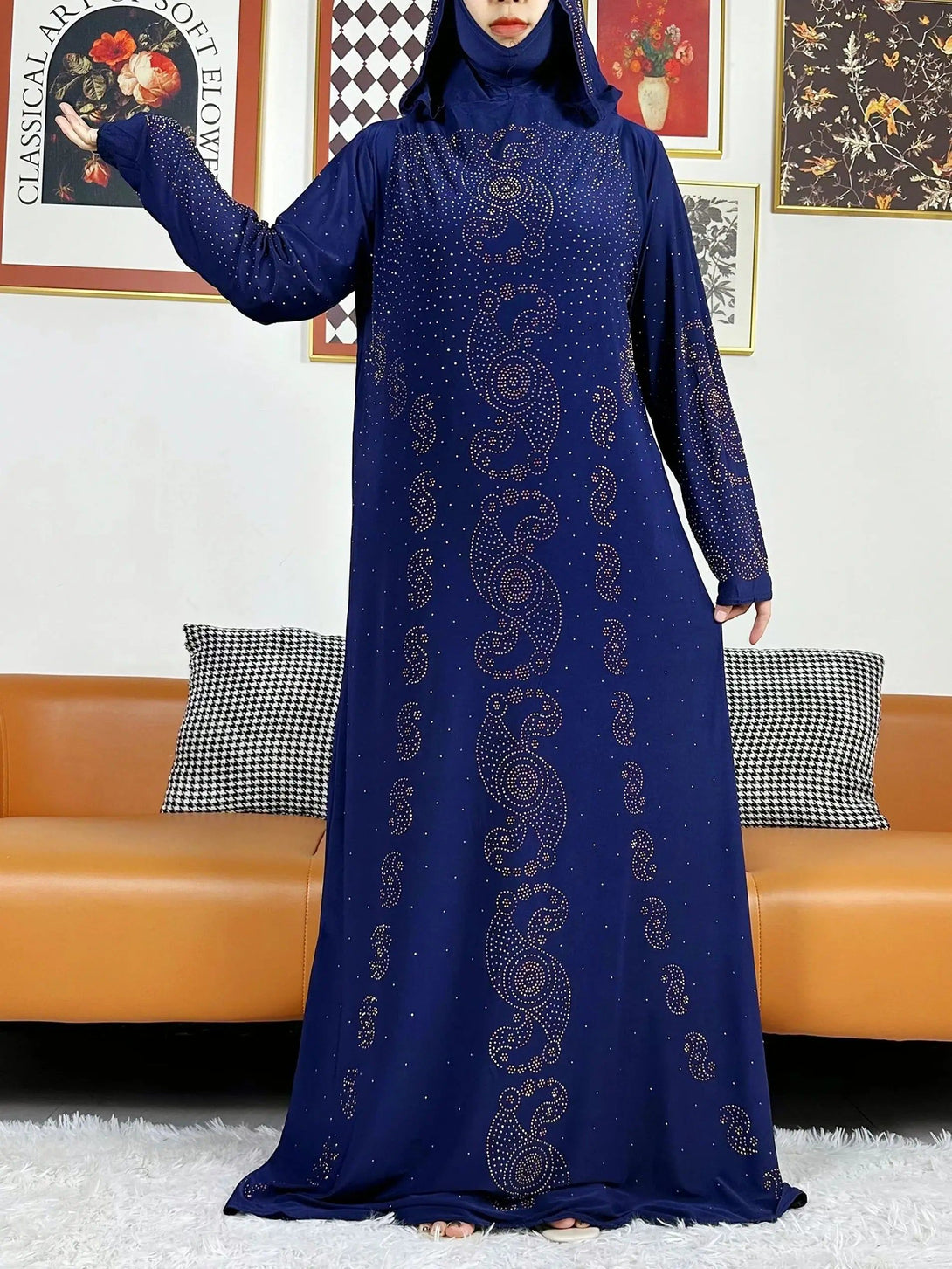 Une robe longue bleu marine à manches longues avec un col rond, des motifs dorés en forme de goutte d'eau et des détails en paillettes. La robe est portée par une femme avec un hijab assorti.