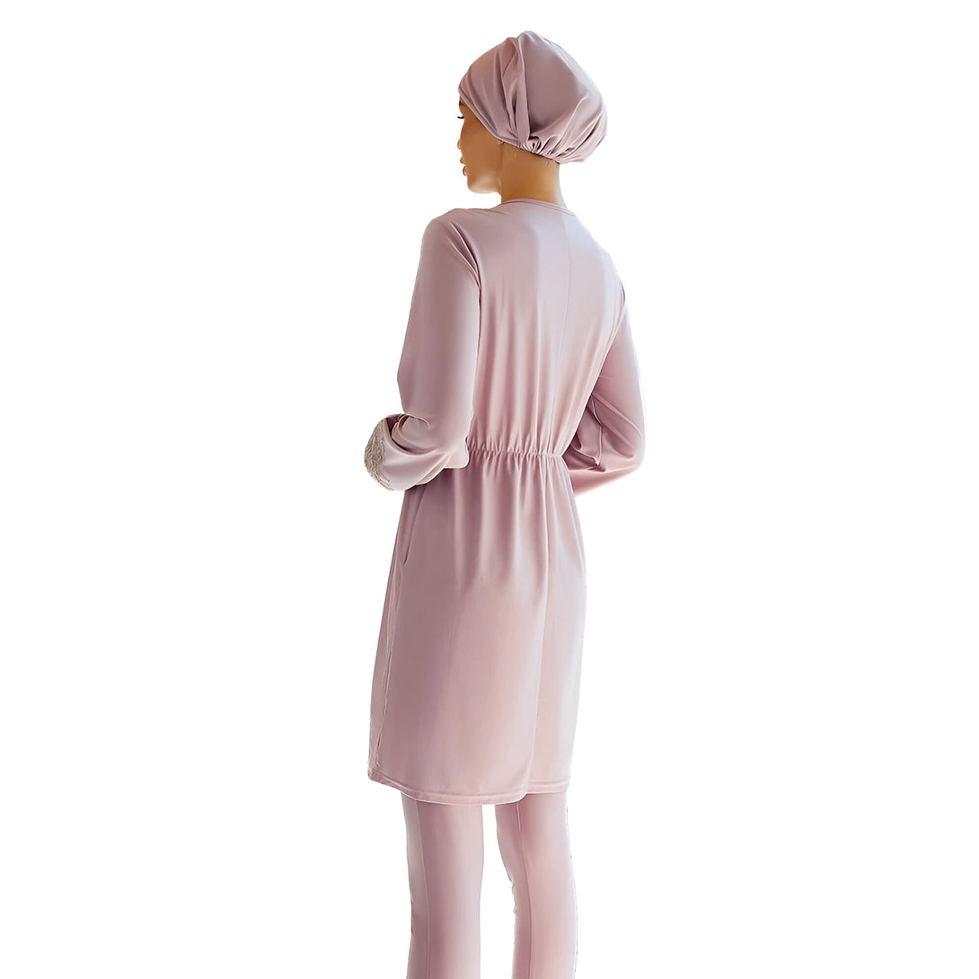 Une femme portant un ensemble de vêtements musulmans rose,  un hijab et une robe longue.  La robe a des manches longues et une ceinture à la taille.
