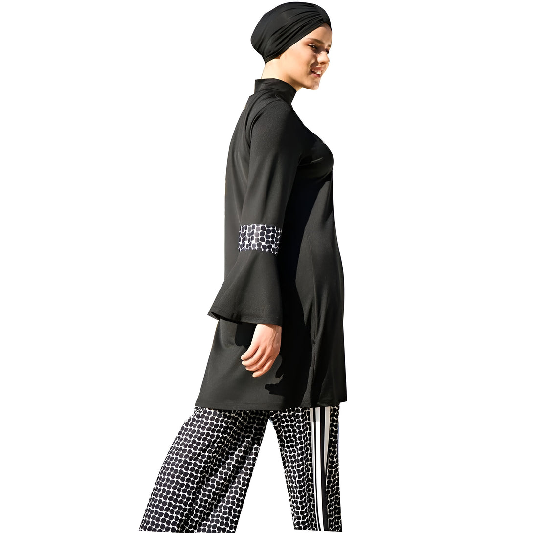 Une femme portant un hijab noir et une tenue de bain musulmane noire avec des détails blancs. La tenue comprend une tunique à manches longues et un pantalon assorti.