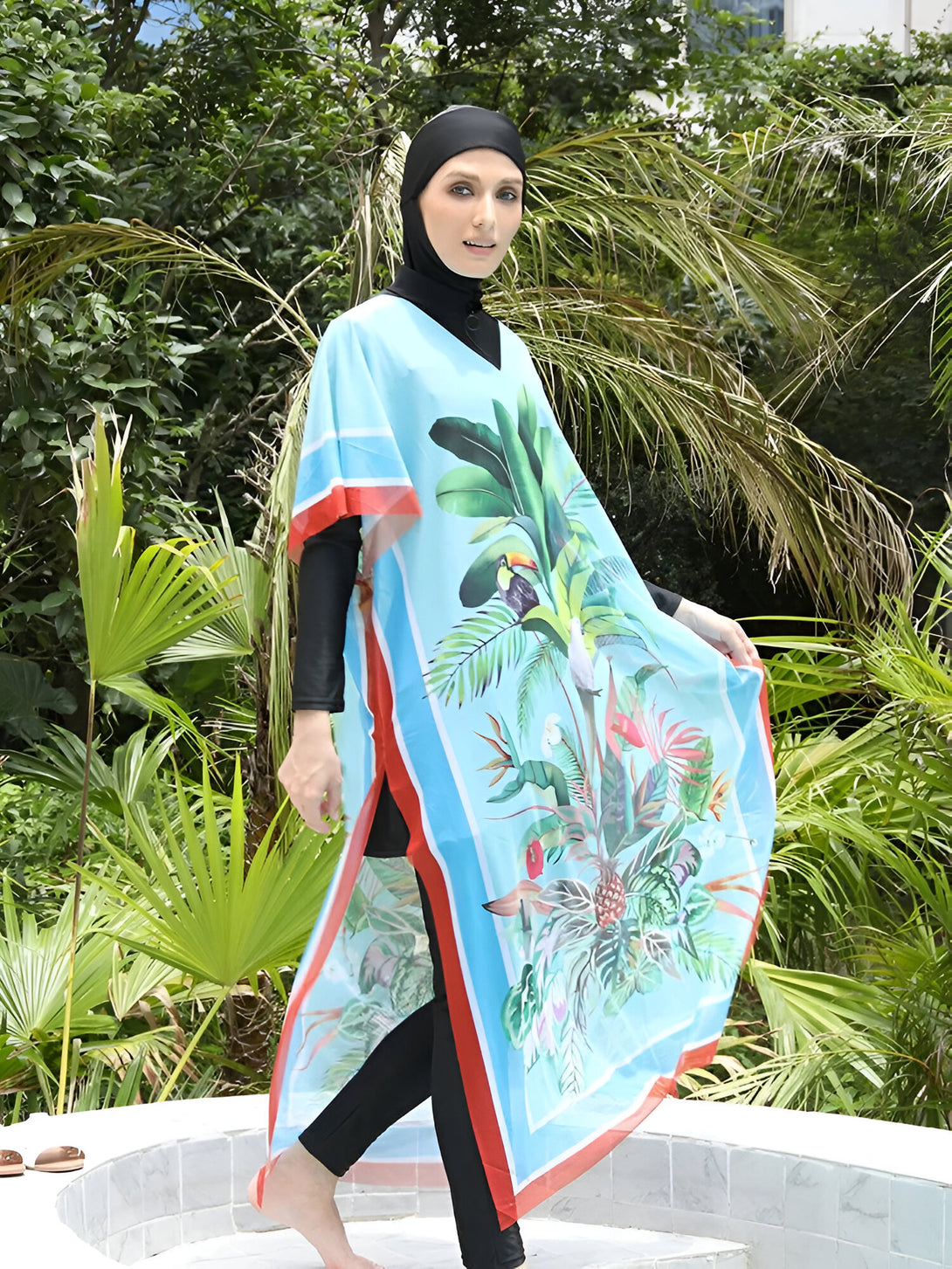 Une femme portant un hijab noir et un maillot de bain musulman bleu avec un motif tropical, se tient près d'une piscine.