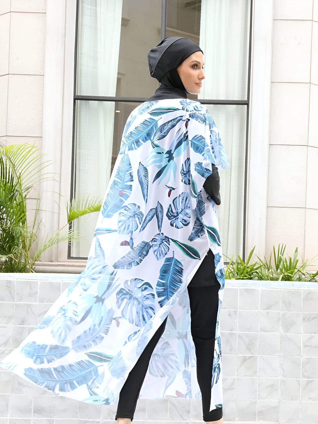 Une femme portant un maillot de bain musulman avec un imprimé tropical, un hijab noir et un pantalon noir.