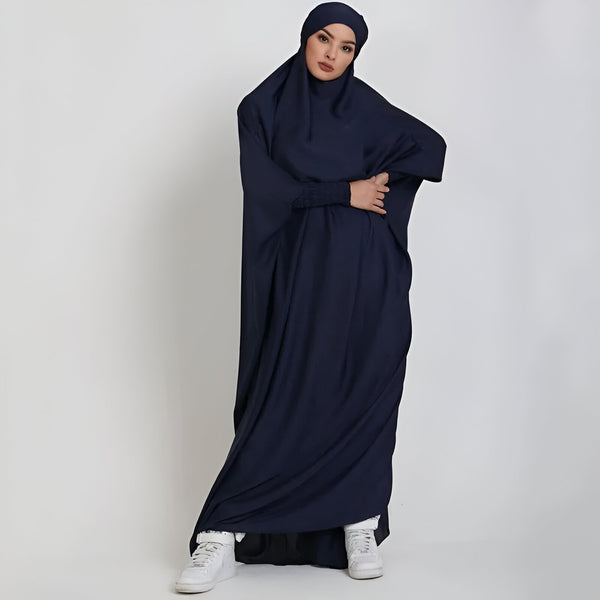 Une femme portant une longue robe bleue à manches longues et un voile assorti. La robe est ample et fluide, idéale pour la prière ou le quotidien.