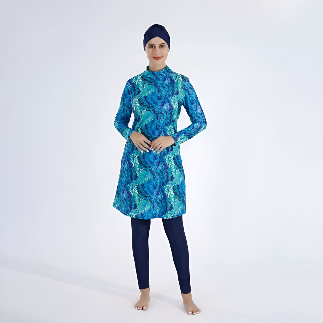 Une femme portant un maillot de bain musulman bleu et vert à motifs de feuilles, avec un hijab bleu foncé.