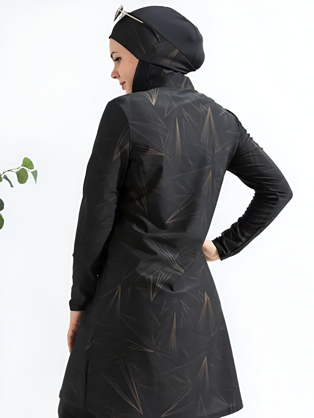 Une femme portant un maillot de bain musulman noir avec un motif géométrique doré. Le maillot de bain est à manches longues et a une jupe longue. La femme porte également un hijab noir.