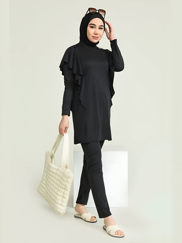 Une femme portant un maillot de bain musulman noir avec une tunique à volants et un pantalon long, tenant un sac à main blanc et portant des sandales.