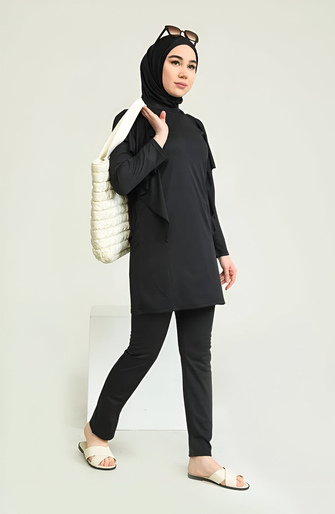 Une femme portant un maillot de bain musulman noir avec un hijab et un sac à main blanc.