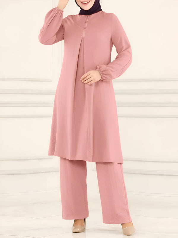Ensemble de vêtements musulmans pour femmes, comprenant une tunique rose à manches bouffantes et un pantalon assorti. La tunique présente une fermeture boutonnée sur le devant et une dentelle délicate. La tenue est élégante et confortable, idéale pour les occasions spéciales ou au quotidien.