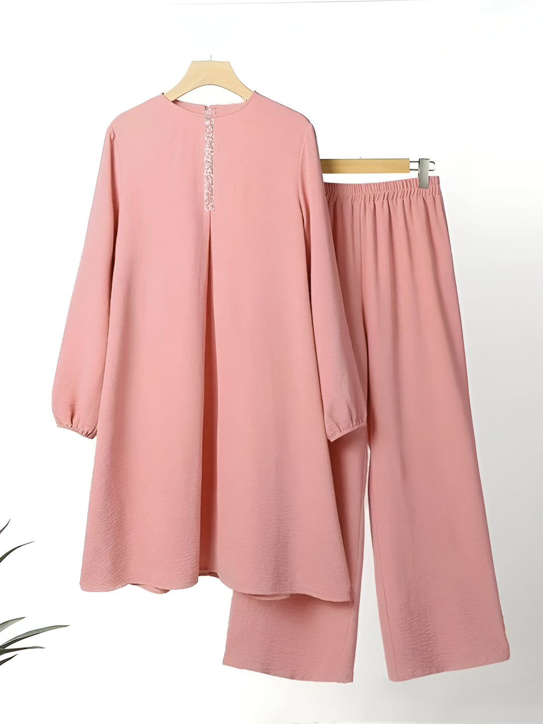 Ensemble de vêtements musulmans rose composé d'une tunique à manches longues et d'un pantalon ample. La tunique a une fermeture boutonnée sur le devant et le pantalon a une taille élastique.