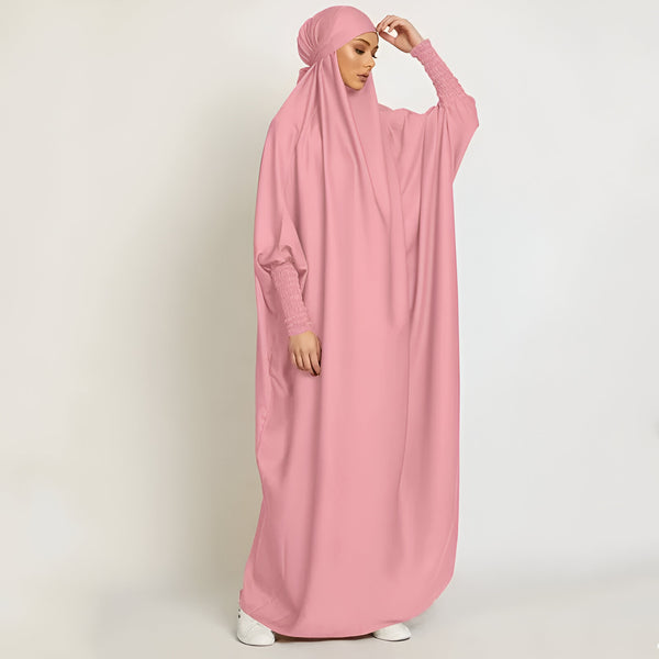Une femme portant une longue robe rose ample avec des manches bouffantes et un voile assorti. La robe est parfaite pour les occasions spéciales ou pour la prière.