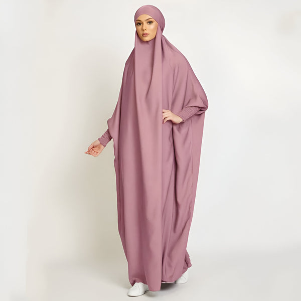 Une femme portant une abaya rose et un hijab assorti, idéale pour les occasions spéciales ou la prière.