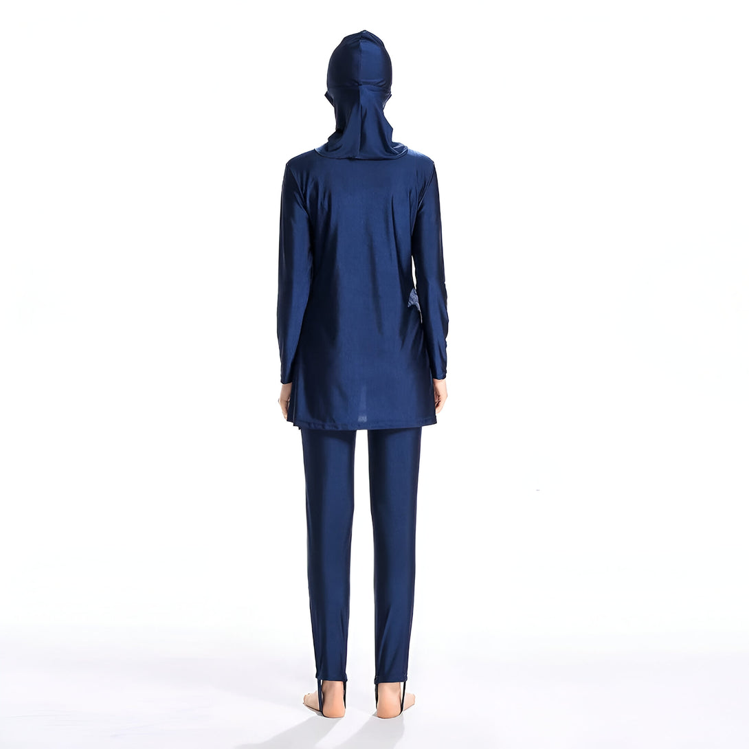 Une femme portant un maillot de bain musulman bleu marine avec une cagoule. Le maillot de bain est à manches longues et comprend un pantalon long. La femme est debout sur un fond blanc.