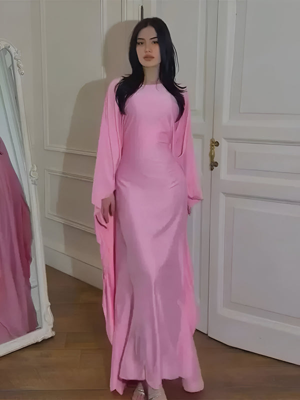 Une femme portant une robe longue rose en satin. La robe a des manches longues et un col rond. La robe est élégante et convient parfaitement aux occasions spéciales.
