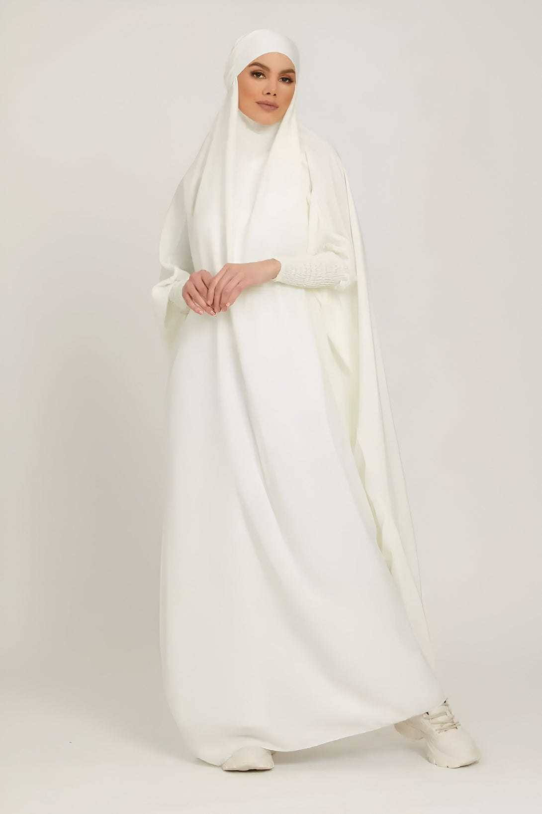 Une femme portant une longue robe blanche musulmane avec un hijab assorti.  Elle porte également des baskets blanches.