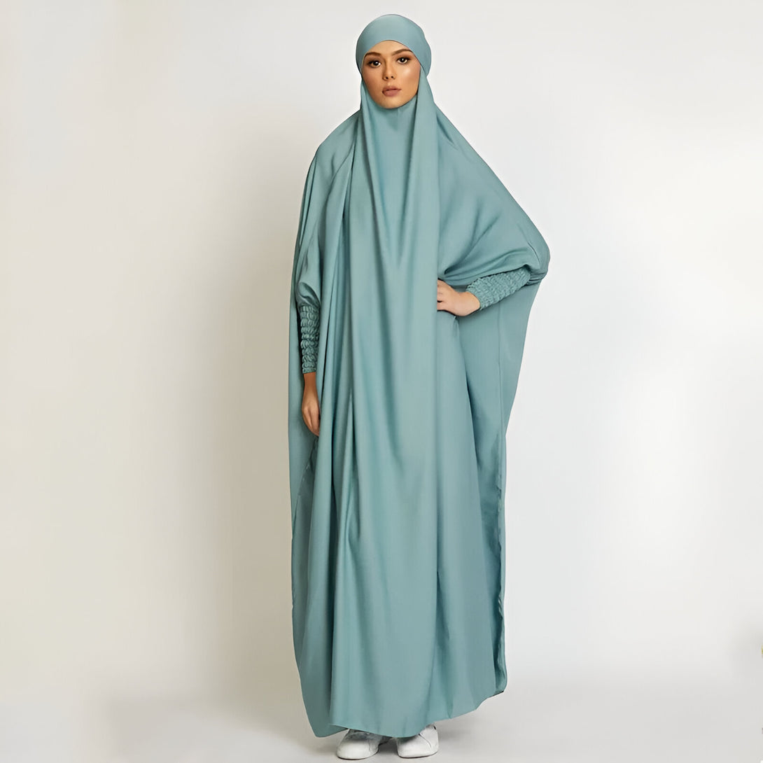 Une femme portant une abaya de prière verte avec un hijab assorti. La robe est ample et confortable, idéale pour la prière.