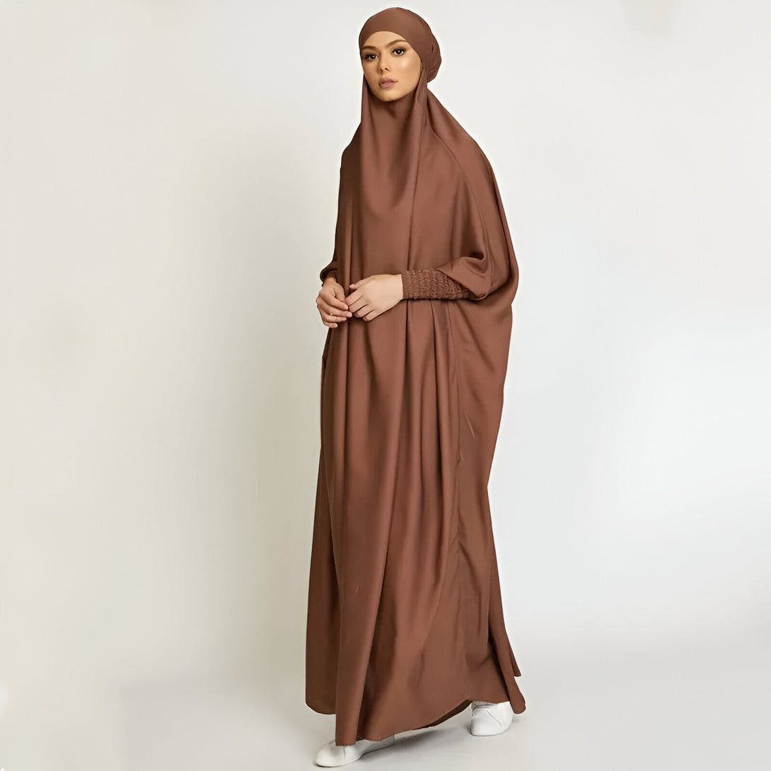 Une femme portant une longue robe marron à manches longues et un hijab assorti. La robe est ample et fluide, idéale pour la prière.