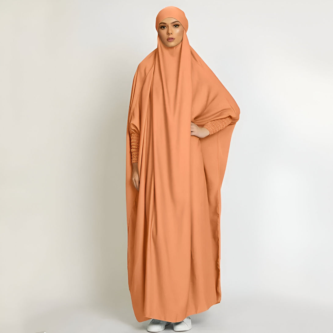 Une femme portant une abaya orange ample avec un hijab assorti. La robe a des manches longues avec des poignets élastiques.