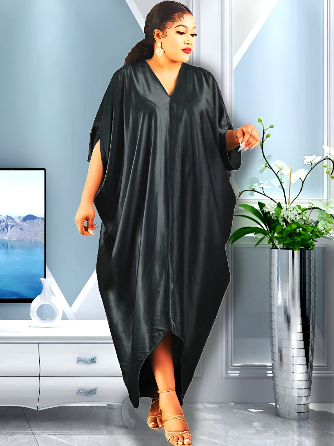 Une femme porte une robe longue noire en satin avec un col en V. La robe est ample et fluide, idéale pour les occasions spéciales ou pour une tenue élégante au quotidien.