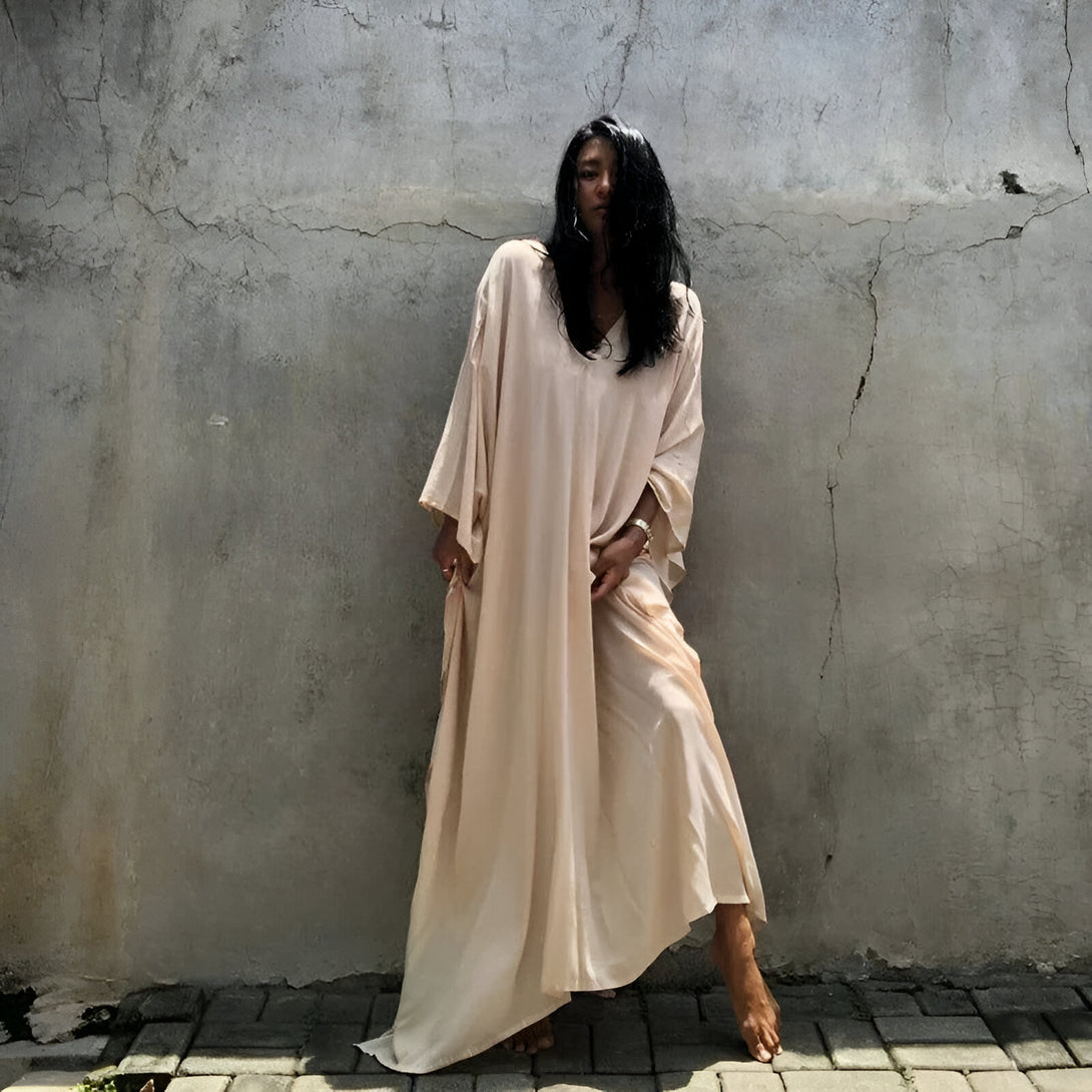 Une femme porte une longue robe beige ample et élégante, idéale pour les occasions spéciales ou pour un look décontracté chic.