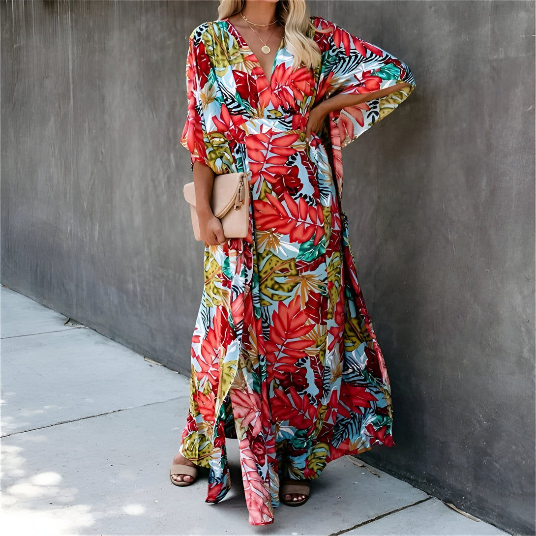 Une femme portant une longue robe d'été à imprimé floral, parfaite pour les occasions spéciales ou les sorties décontractées. La robe est ample et fluide, avec un décolleté en V et des manches 3/4. La robe est disponible en plusieurs couleurs et tailles.