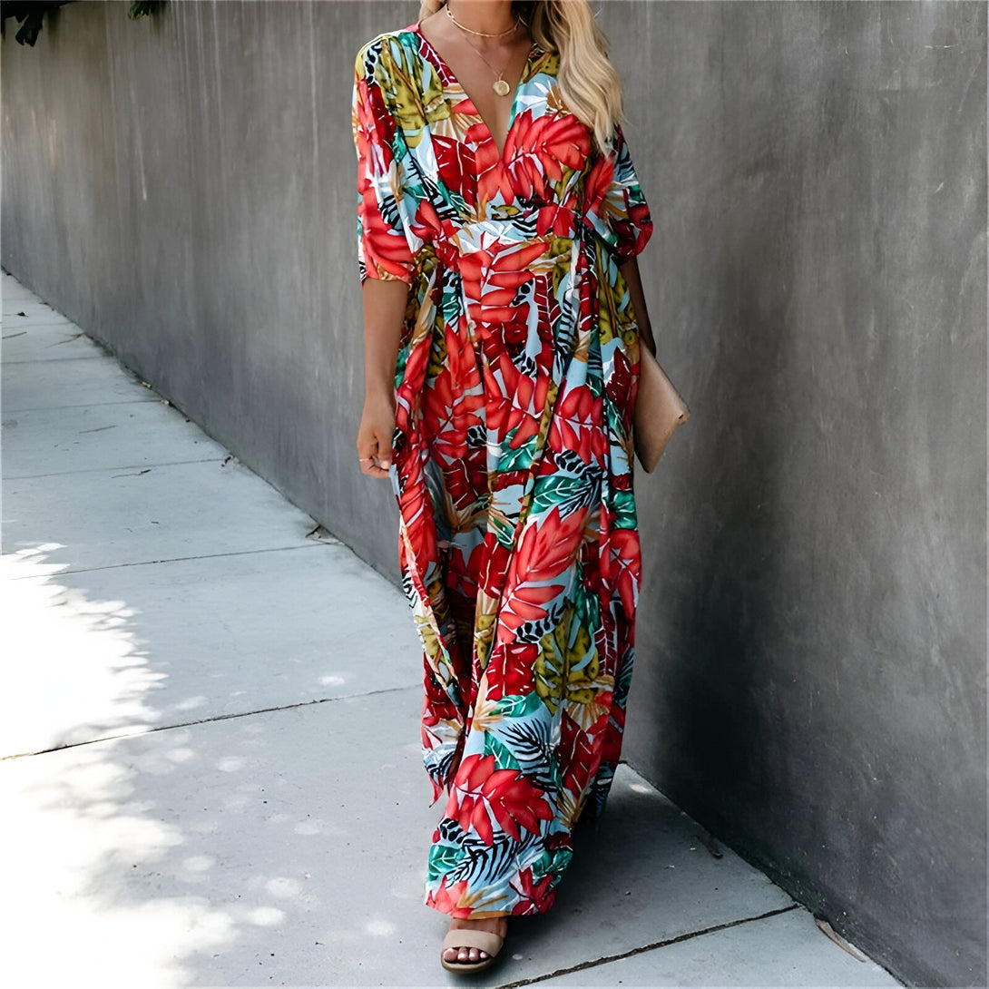 Une femme porte une longue robe à imprimé floral rouge et bleu. La robe a une encolure en V et des manches trois-quarts. La robe est parfaite pour les occasions décontractées et les vacances.