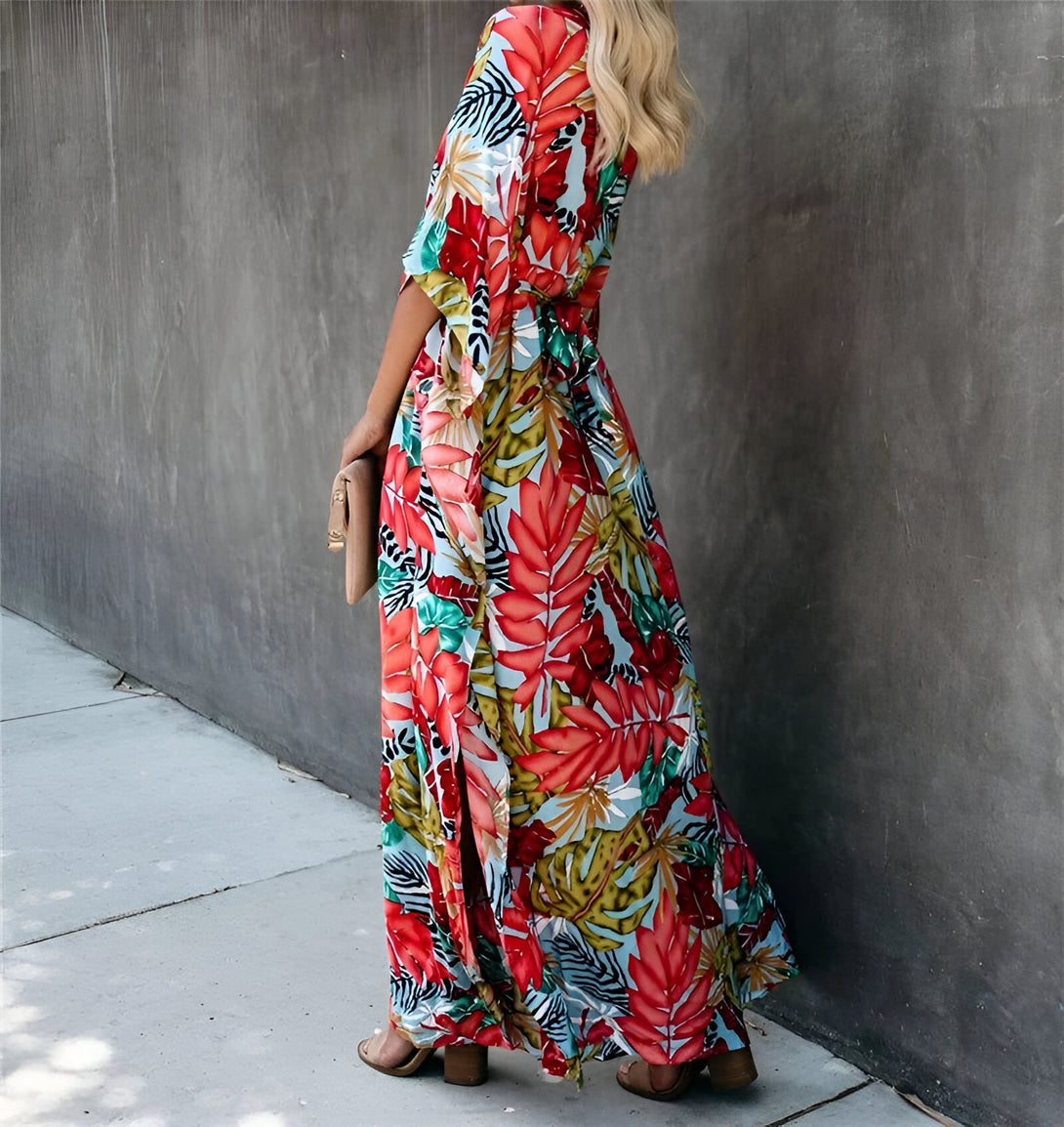 Une femme portant une longue robe de plage à fleurs avec une fente sur le côté. La robe est de couleur bleu clair et rouge avec des imprimés tropicaux.