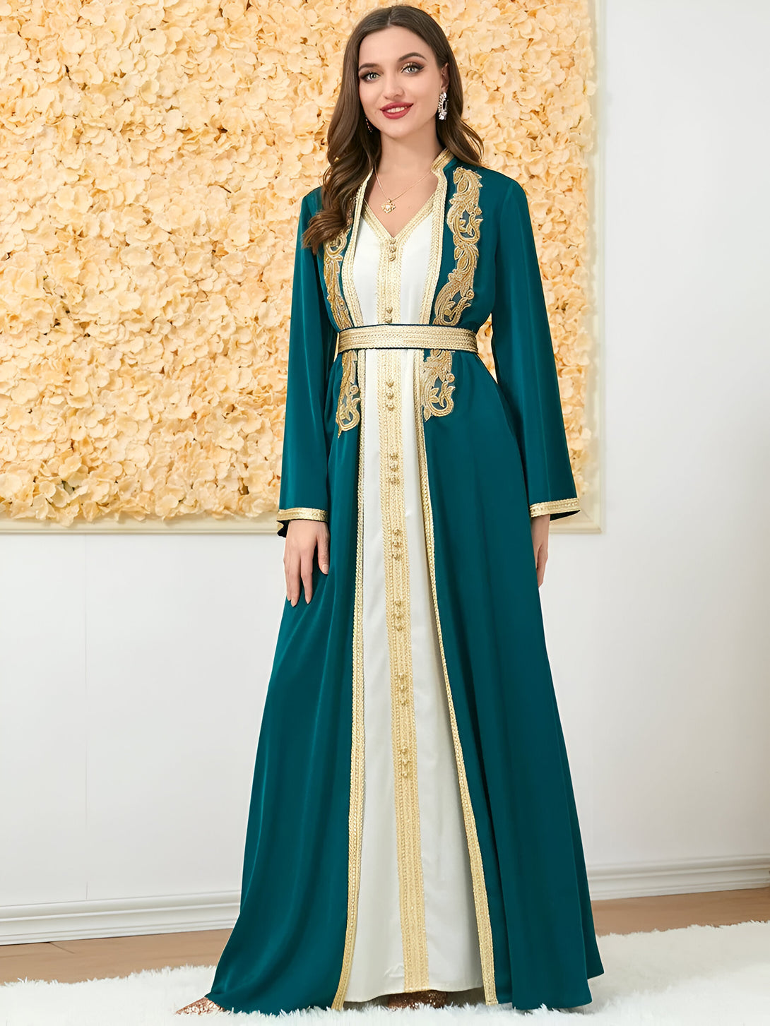Une femme porte une robe longue verte avec des broderies dorées. La robe est cintrée à la taille et a un col en V.