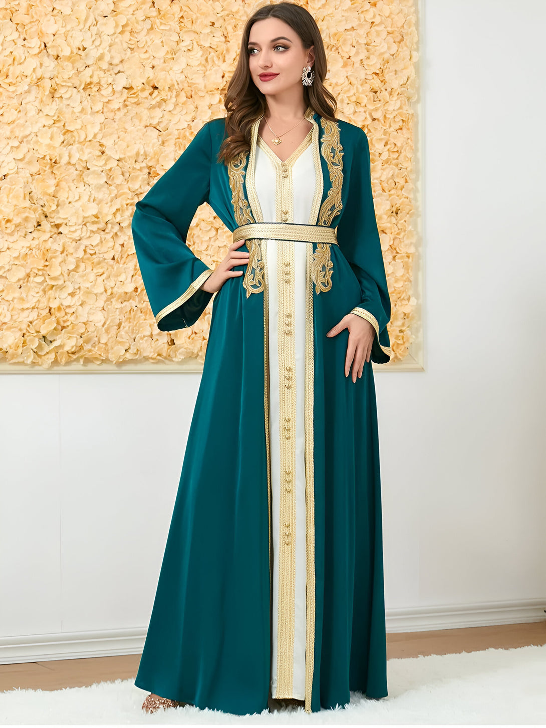 Une femme porte une robe longue verte à manches longues avec des broderies dorées. La robe est cintrée à la taille et a une fente sur le devant.